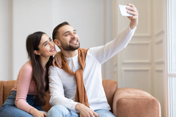 istock Cheerful Arab Couple Making Selfie On Mobile Phone At Home 1322921001