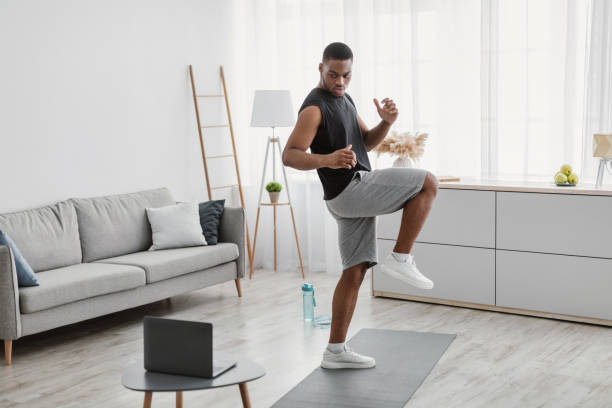 istock African Guy Doing Standing Knee Raise Exercise At Laptop Indoor 1322921002
