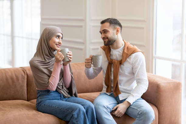istock Cheerful Muslim Spouses Drinking Coffee Sitting On Couch Indoors 1322921062
