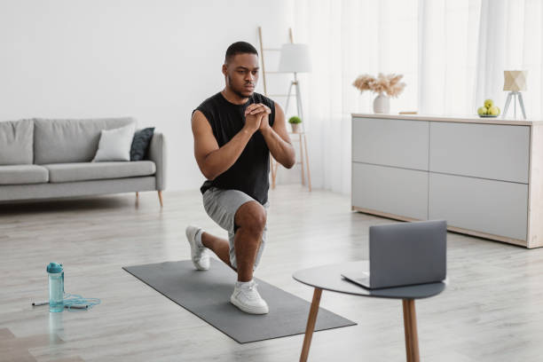 istock Determined African Guy Exercising At Laptop Doing Forward Lunge Indoor 1322921067