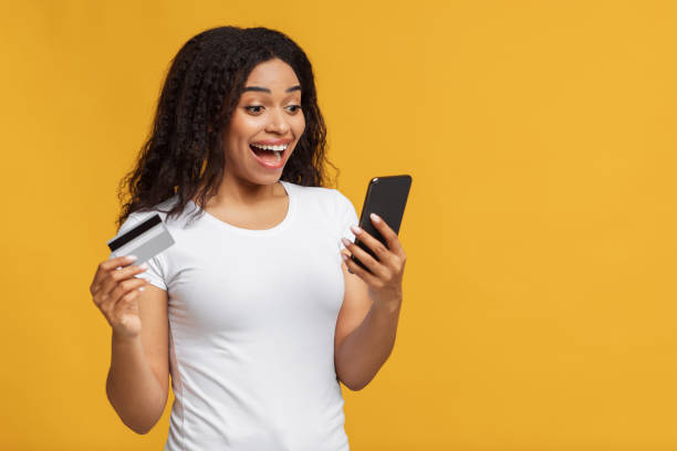 istock Mobile application for shopping. Overjoyed african american lady making online order, using smartphone and credit card 1322921156