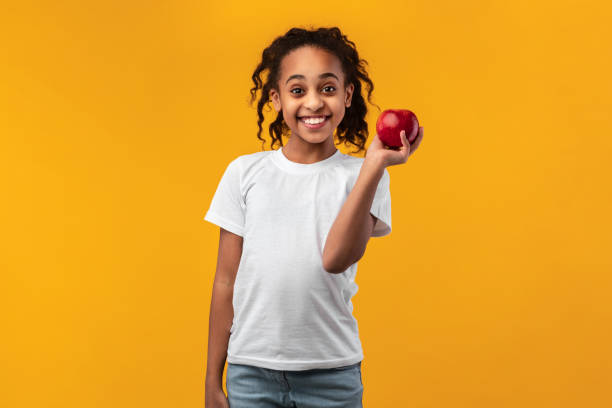 портрет веселой черной девушки, держащей красное яблоко - apple healthy eating eating black стоковые фото и изображения