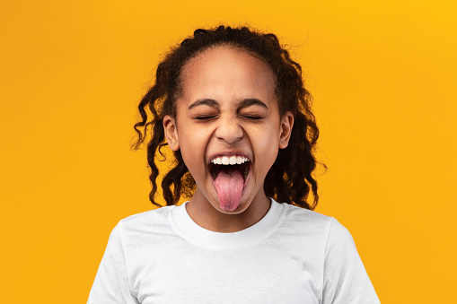 Human Emotions, Reactions And Attitude Concept. Closeup portrait of African American girl showing sticking out her tongue at camera, playing and having fun. Goofy kid fooling around