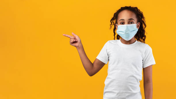 istock Black girl in mask pointing aside at free copy space 1322922278