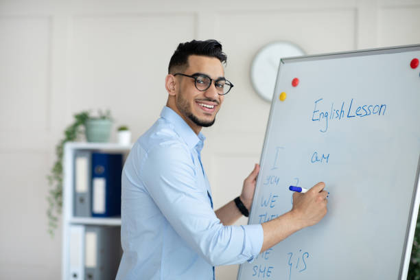 istock Young Arab male teacher giving online class, explaining new material, writing English rules on blackboard at home office 1322922394