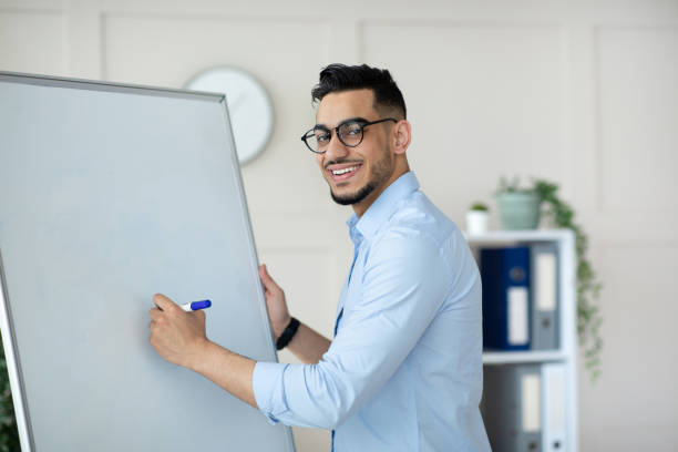 istock Young Arab male tutor conducting online lesson near empty blackboard, writing down info during webinar at home 1322922420