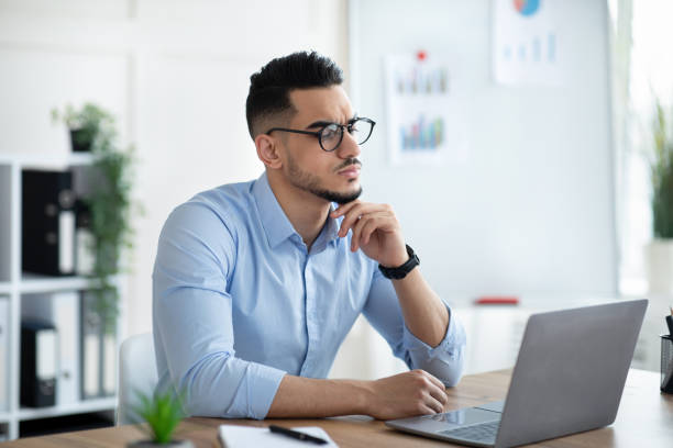 istock Troubled Arab businessman sitting at his desk, looking at laptop screen, solving work problem in modern office 1322922440