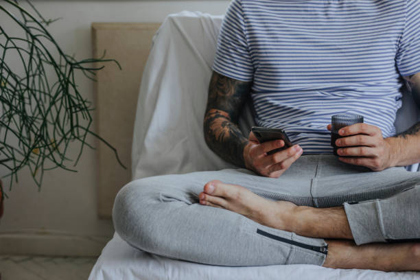 istock Casual Anonymous Young Man Using his Smartphone at Home while Sitting Down and Having a Drink 1322923403