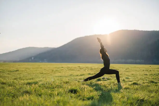 Photo of Young woman practices yoga in grassy meadow at sunrise