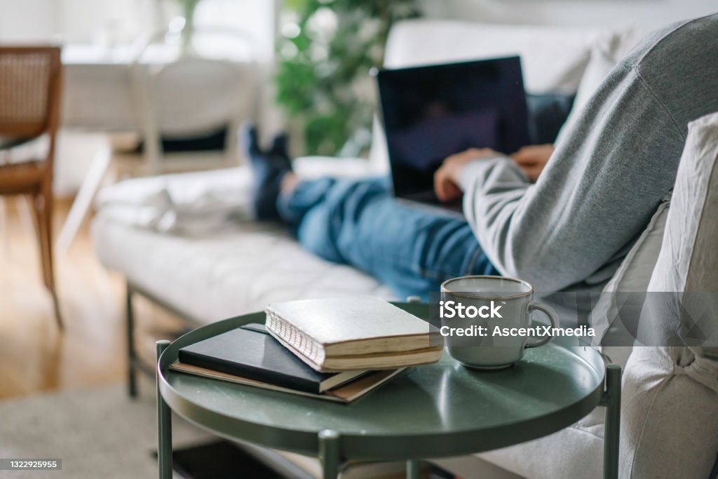 Young man works online from living room He relaxes at home during quarantine and works on laptop Coffee Table Stock Photo