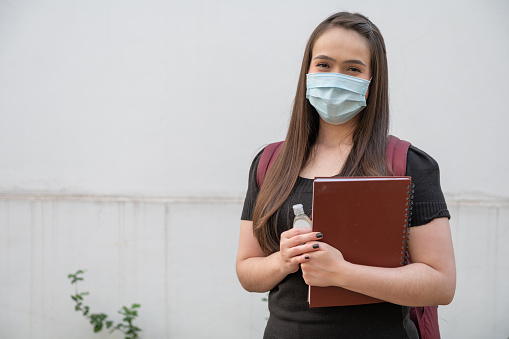 Portrait of a college student Wearing protective face Mask While Standing With Books