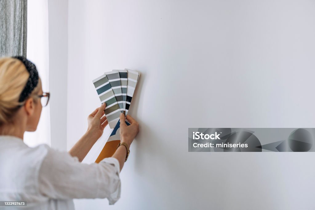 Young Woman Holding Colour Chart On White Wall Unrecognizable creative young architect looking at colour catalogue choosing paint palette for home interior and walls Color Swatch Stock Photo