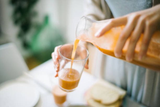 Young woman pours a glass of carrot-orange juice To enjoy with continental breakfast at home vitamin a nutrient stock pictures, royalty-free photos & images