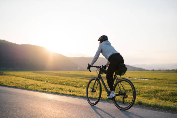 junge frau radelt bei sonnenaufgang auf landstraße - ideas concepts power sunrise stock-fotos und bilder