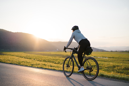 Young woman bikes down country road at sunrise