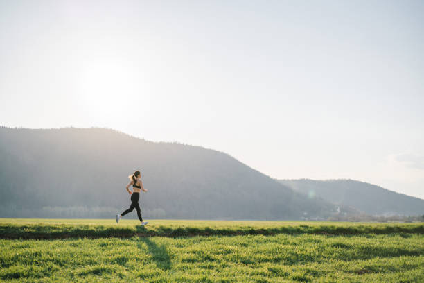 若い女性は日の出時に田舎道を走る - distant field meadow landscape ストックフォトと画像