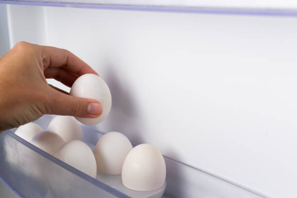 A hand puts an egg into a mold on the refrigerator door. stock photo