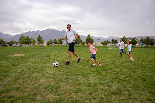 A father plays soccer with his two kids at a public park in Draper, Utah.