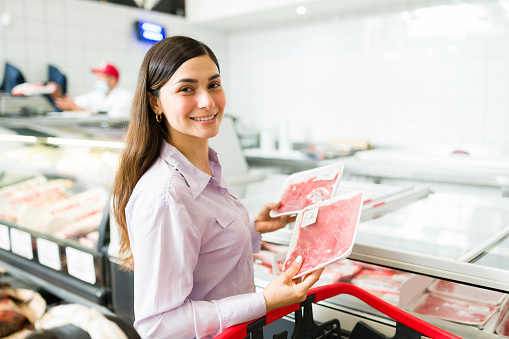 Quick grocery trip at the supermarket. Beautiful latin woman holding packed raw meat and choosing fresh food to buy at the grocery store