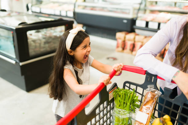 Annoyed young daughter shouting in the store Angry little kid screaming and throwing a tantrum while grocery shopping with her mom at the supermarket because she won't buy her candy displeased stock pictures, royalty-free photos & images