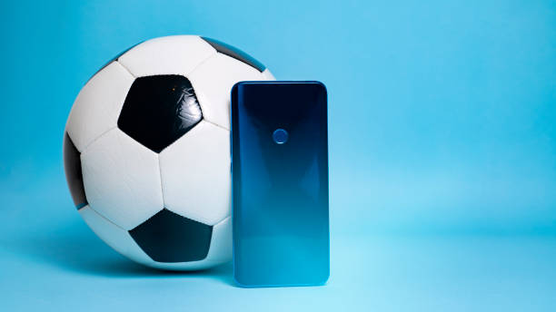 istock Smartphone next to soccer ball on blue background 1322937067