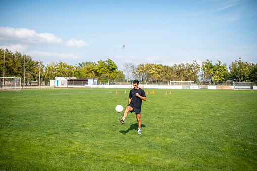 Mature Caucasian male footballer juggling ball on sports field while practicing ball control.