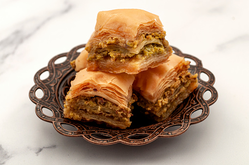 Authentic Middle Easter desserts concept with close up on Turkish baklava on small metal plate beautifully orate with Arabic ornaments isolated on white background with clipping path cutout