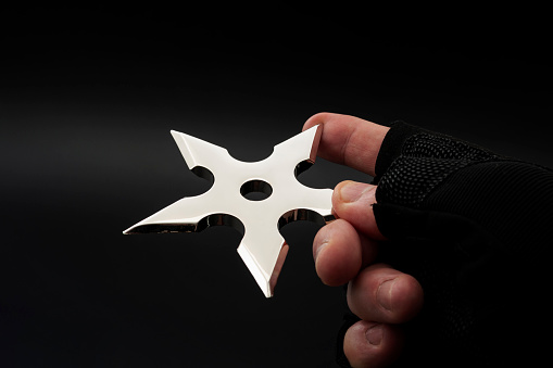 Martial arts skill and traditional Japanese weapon concept with hand in fingerless ninja glove trowing metal star shaped shuriken isolated on black background with copy space