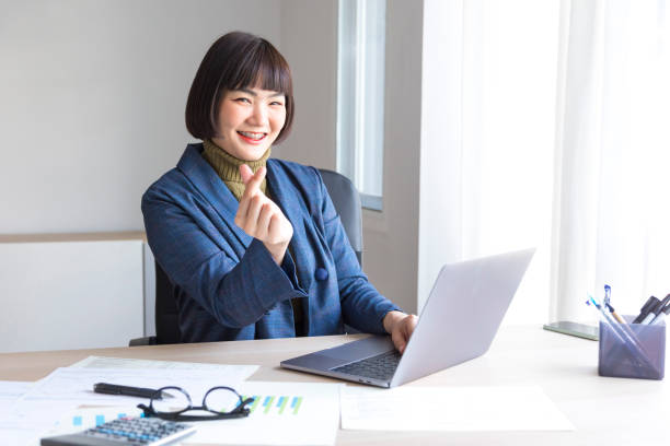 istock Asian female entrepreneur sitting at table and browsing laptop while looking at camera and showing thumbs up. 1322943520