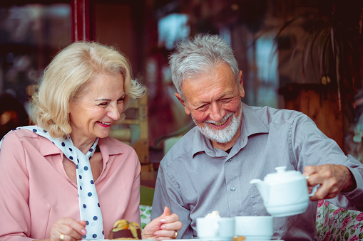 An image presenting an adorable elderly couple relaxing at the local cafeteria decorated in retro style. They're having a conversation and drinking tea.