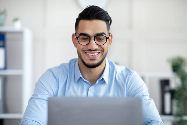 istock Young Arab businessman with laptop working online, making presentation at modern office 1322962938