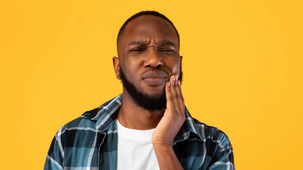 unglücklicher schwarzer mann leidet unter zahnschmerzen über gelbem hintergrund - abszess stock-fotos und bilder