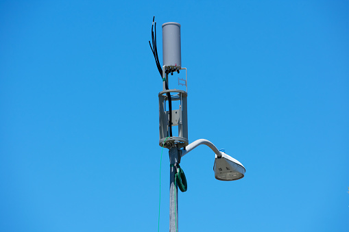 A small cell antenna installation on a lamp post is in progress. Protective antenna shroud removed, equipment parts are visible and various cables are hanging in the air.