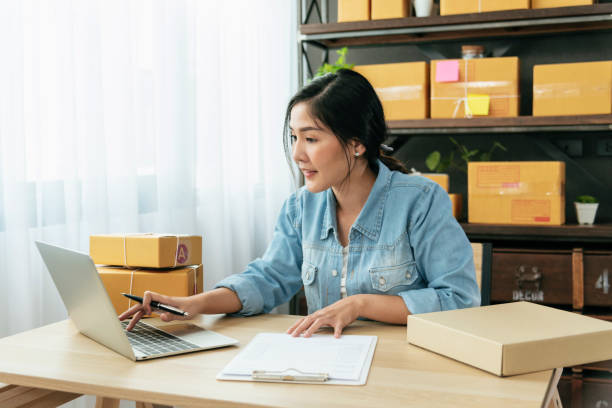 vendedor online feche as mãos jovem asiática digitando teclado portátil verificando pedido on-line, verifique pacote de entrega de mercadorias entregando postal. mulher asiática startup pequeno negócio em home office - pequenas empresas - fotografias e filmes do acervo