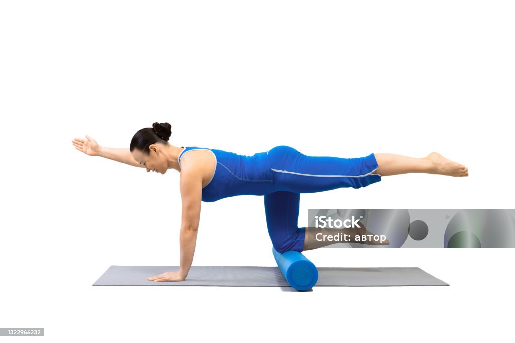 Adult fit woman does bird dog drill with one leg and arm up and foam roller under her knees. Classic pilates exercise, isolated on white. Adult fit woman does bird dog drill with one leg and arm up and foam roller under her knees. Classic pilates exercise, isolated on white. Pelvic floor, promo, female workout, wellness, balance, focus, health concept. Pelvic Floor Stock Photo