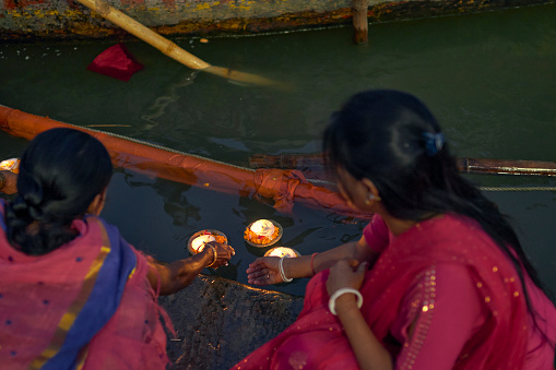 Varanasi, 11/16/2018 : Two female tourist in ethnic dress floating decorated diyas in holy Ganges water at Dasaswamedh Ghat in evening. This ritual symbolises the worship of holy Ganges river by Hindu devotees.