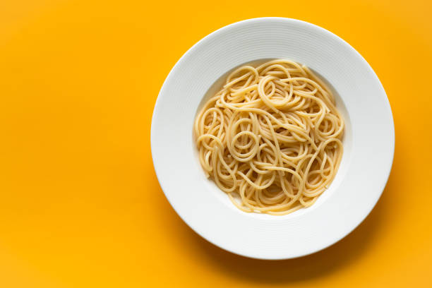 High angle view of plain cooked spaghetti in white ceramic plate High angle view of plain cooked spaghetti in white ceramic plate, on orange background, copy space. spaghetti stock pictures, royalty-free photos & images