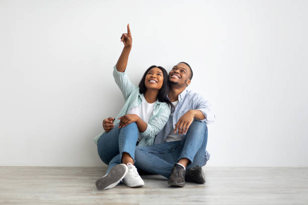 istock Advertisement for loan. Dreaming black couple sitting on floor and pointing at empty space above them 1322973176
