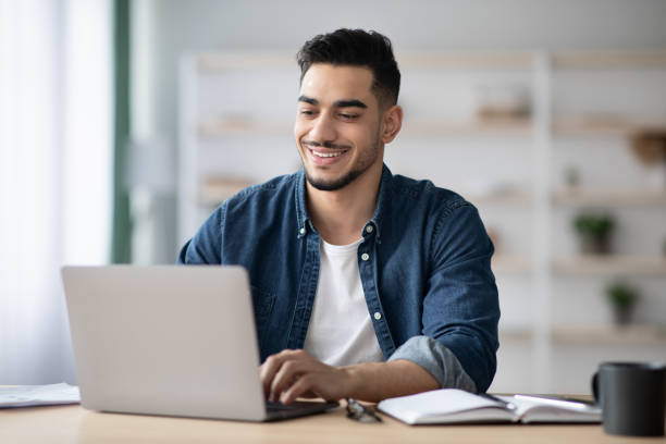 istock Cheerful arab guy working on laptop, typing on keyboard 1322973274