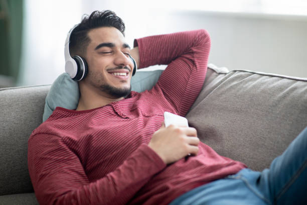 istock Positive arab guy enjoying music, using mobile phone and headset 1322973311