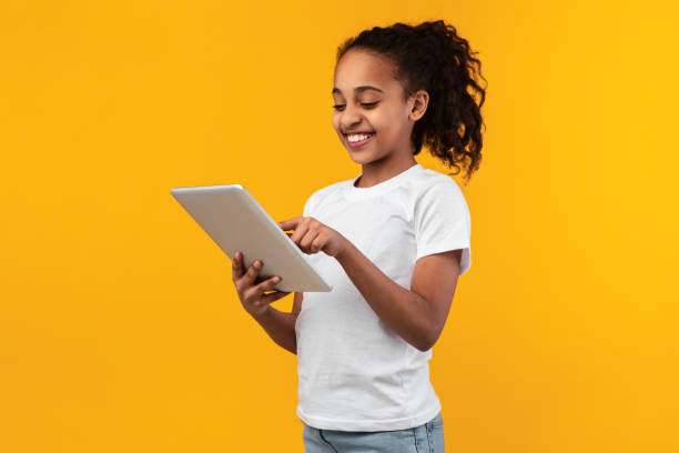 istock Black girl standing with tablet at yellow studio 1322973325