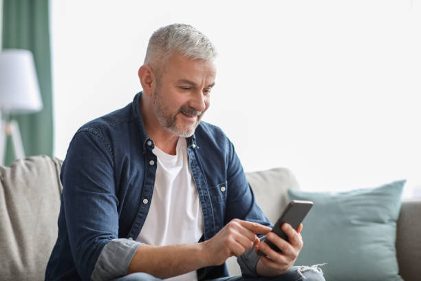 istock Smiling senior man using smartphone at home 1322973336