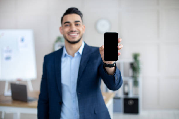 istock Positive Arab businessman holding smartphone with empty screen at office, mockup for mobile app or website design 1322973624