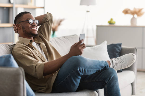 istock Cheerful Black Man Using Cellphone Wearing Eyeglasses At Home, Side-View 1322974343