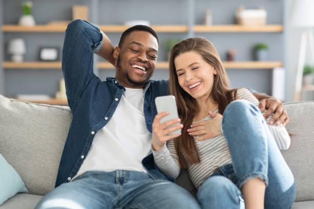 istock Cheerful Interracial Lovers Watching Funny Videos On Smartphone At Home 1322975421