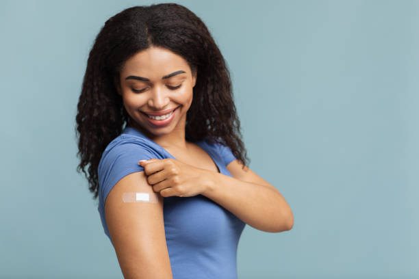 istock Coronavirus vaccination advertisement. Happy vaccinated black lady showing arm with plaster over blue background 1322975544