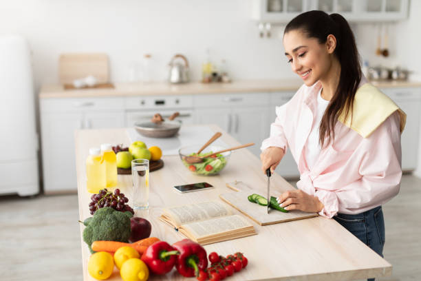 Woman cooking salad and using cookbook at kitchen