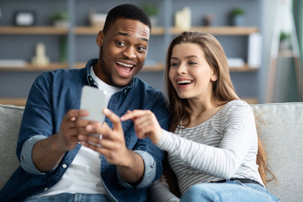 istock Excited Multicultural Couple Using Smartphone Together While Relaxing On Couch At Home 1322976715