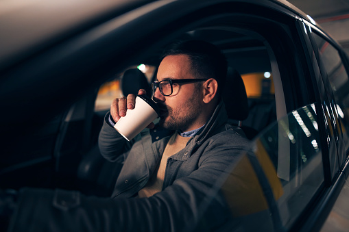 Attractive successful man sitting at his car driving and drinking coffee to go