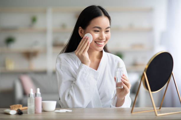 mujer asiática alegre limpiando su cara con tóner - facial cleanser fotografías e imágenes de stock